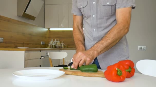 Affettare peperone verde sul tagliere di legno. Maschio taglia capsicum a mano con coltello. L'uomo sta tagliando le verdure dolci. Note di alimentazione, dieta, cucina a casa — Video Stock