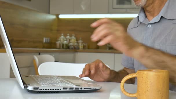 Senior man is typing on keyboard of laptop, businessman is using digital tablet at home at the kitchen, account manager working, remote job — Stock video