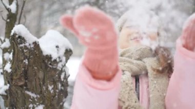 Pembe montlu, bej şapkalı ve eldivenli bir kızın kış ormanı ve karlı havada oynadığı kış portresi. Mutlu çocukluk ve aktif tatil kavramı