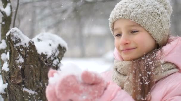 Winterporträt eines kleinen Mädchens in rosa Mantel mit beigem Hut und Fäustlingen, die draußen im verschneiten Winterwald spielen und Schnee pusten. Glückliche Kindheit und aktives Ferienkonzept — Stockvideo