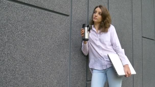 은색 랩탑 과 커피 잔을 들고 어두운 회색 벽 근처에서 아침을 기다리고 있는 젊은 여성의 여성 사진, 멀리 떨어진 직업, 커피 휴식, 똑똑 한 학생 개념 — 비디오