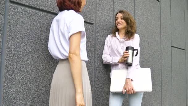 Två framgångsrika affärskvinnor talar om ett projekt när de står nära väggen utanför med en bärbar dator under en paus från jobbet — Stockvideo