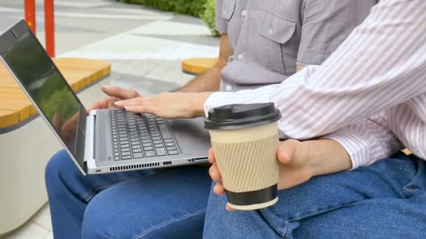 Empleada joven está enseñando a su colega mayor cómo utilizar el ordenador portátil y el software corporativo sentado en el banco fuera de la oficina, coorporate pasantía, asociación educativa. — Vídeos de Stock