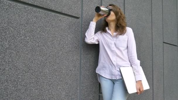 Vrouwelijke portret van jonge vrouw met zilveren laptop en kopje koffie te wachten op een vergadering in de buurt van donkergrijze muur in de ochtend, afgelegen baan, koffiepauze, slimme student concept — Stockvideo