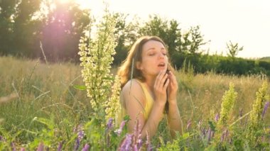 Güzel bir genç kız, yaz boyunca elinde çiçeklerle tarlanın ortasında oturuyor ve hapşırıyor, aşırı duyarlılık, astım ya da alerji konsepti.