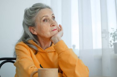 Gri saçlı ve kırışık yüzlü güzel yaşlı büyükanne pencere arkasında bir şey düşünüyor, anneler günü, mutlu emeklilik.