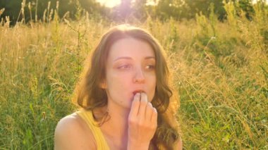 Yaz pikniği sırasında olgun çilek yiyen güzel bir kızın portresi ya da gün doğumunda çayır, havada sinekler uçuşuyor.