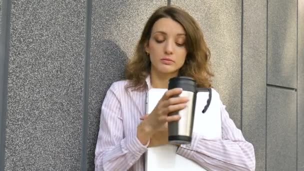 Žena portrét mladé ženy se stříbrným notebookem a šálkem kávy čeká na setkání u tmavě šedé stěny v dopoledních hodinách, vzdálená práce, káva ebreak, chytrý studentský koncept — Stock video