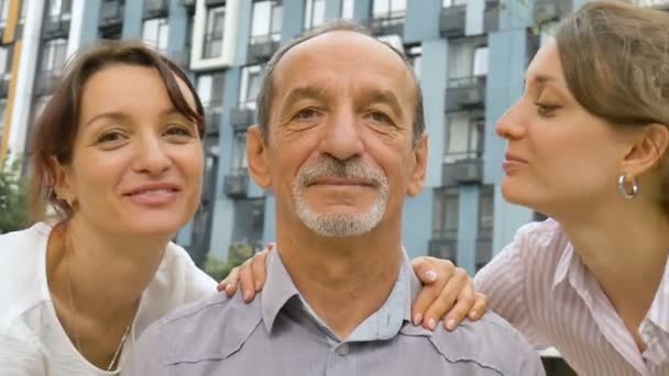 Familie portret van senior vader en twee volwassen dochters zoenen hem buiten op moderne gebouw van nieuwe residentiële complex, vaders dag viering concept — Stockvideo