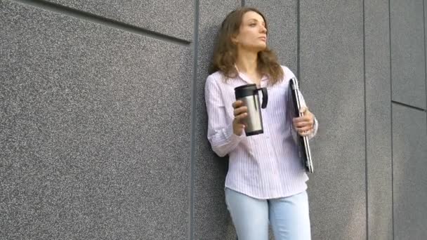 Kvinnligt porträtt av ung kvinna med silver laptop och kopp kaffe väntar på ett möte nära mörkgrå vägg på morgonen, distansarbete, fikapaus, smart student koncept — Stockvideo