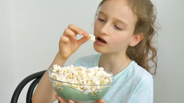 Retrato de uma estudante engraçada e animada em um fundo branco, sorrindo e comendo pipocas de uma tigela — Vídeo de Stock