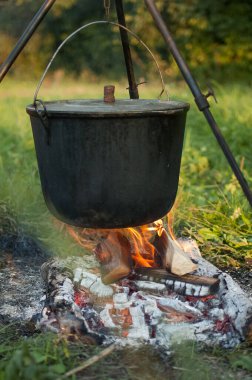 Koyu büyük tencere ya da kazan, ateşin içinde kaynar suyla pişirme tavası, parkta ya da dağlarda bir yerde, kamp konsepti.