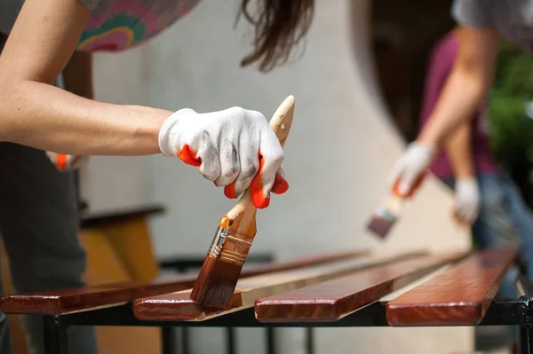 Жінка-працівник робить роботи з фарбування дерев'яних виробів, дошку з коричневою фарбою для виготовлення лавки, теслярів, захист дерев'яного покриття . — стокове фото