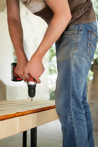 Abilità giovane lavoratore maschile sta utilizzando cacciavite di potenza di perforazione durante la costruzione banco di legno, fai da te — Foto Stock