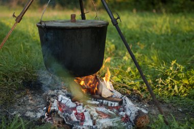Koyu büyük tencere ya da kazan, ateşin içinde kaynar suyla pişirme tavası, parkta ya da dağlarda bir yerde, kamp konsepti.
