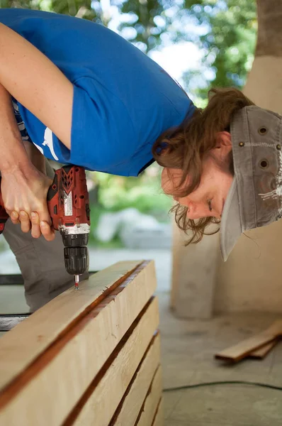 Кваліфікована молода жінка-працівник використовує буріння силової викрутки під час будівництва дерев'яної лави гендерної рівності, фемінізму, робить це самостійно . — стокове фото