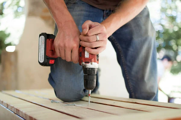 Trabajador masculino joven calificado está utilizando la perforación del destornillador de potencia durante la construcción banco de madera, hágalo usted mismo — Foto de Stock