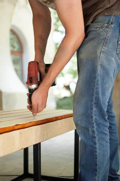 Abilità giovane lavoratore maschile sta utilizzando cacciavite di potenza di perforazione durante la costruzione banco di legno, fai da te — Foto Stock