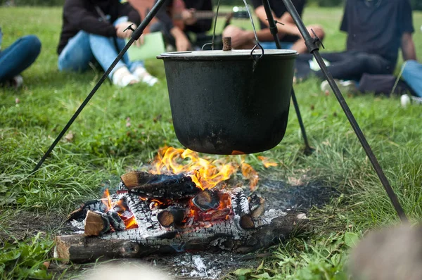 Mörk stor gryta eller gryta, kokpanna med kokande vatten inne ovanför brasan någonstans i parken eller bergen, campingkoncept Stockbild