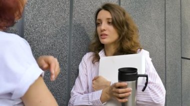 İki başarılı iş kadını bir proje hakkında konuşuyorlar. dışarıda duvarın yanında bir dizüstü bilgisayarla duruyorlardı.