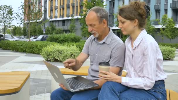 Jonge werknemer leert haar oudere collega laptop en bedrijfssoftware te gebruiken op de bank buiten het kantoor, cooorporate intership, education partnership. — Stockvideo