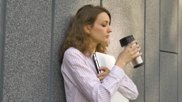 Kvinnligt porträtt av ung kvinna med silver laptop och kopp kaffe väntar på ett möte nära mörkgrå vägg på morgonen, distansarbete, fikapaus, smart student koncept — Stockvideo