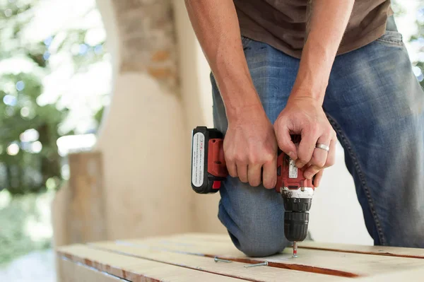 Abilità giovane lavoratore maschile sta utilizzando cacciavite di potenza di perforazione durante la costruzione banco di legno, fai da te — Foto Stock