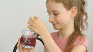 Tatlı küçük kız ahududu kokteyli içip gülümsüyor. Vejetaryen içeceği. Taze ahududu suyu ve sağlıklı beslenmeyi seven bir çocuğun yakın plan portresi.