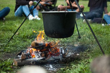 Koyu büyük tencere ya da kazan, ateşin içinde kaynar suyla pişirme tavası, parkta ya da dağlarda bir yerde, kamp konsepti.