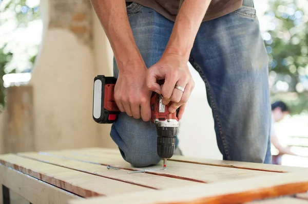 Abilità giovane lavoratore maschile sta utilizzando cacciavite di potenza di perforazione durante la costruzione banco di legno, fai da te — Foto Stock