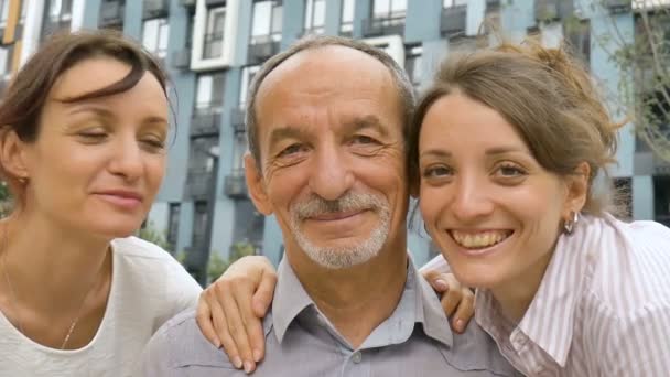 Retrato familiar del padre mayor y dos hijas adultas besándolo al aire libre en el edificio moderno del nuevo complejo residencial, concepto de celebración del día del padre — Vídeo de stock