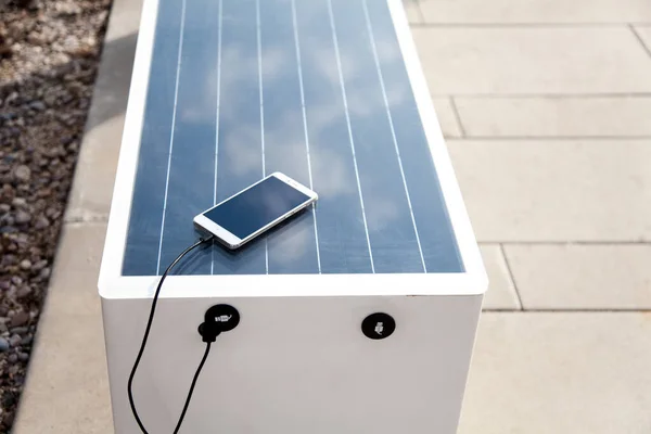 Solar panel on bench. Mobile phone charging via USB from solar power outdoors. Alternative electricity source. Concept