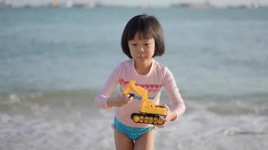 Asyalı Çinli kız çocuk deniz kenarında plastik oyuncak kazıcısıyla oynuyor.