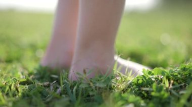 Bir çocuğun ayaklarının yavaş çekimde çimlerin üzerinde yürümesi ve sonunda piknik paspasında oturması.