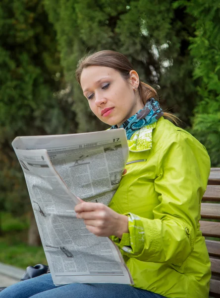 Жінка читає газету, сидячи на лавці — стокове фото