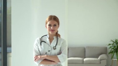 Hastane ofisinde poz veren gülümseyen kadın doktor. Beyaz önlüklü beyaz kadın doktor kameraya bakıyor.