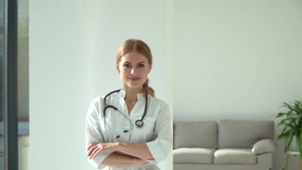 微笑的女医生在医院的办公室里摆姿势。快乐的年轻的高加索女医生，身穿白色的医疗服，看着相机 — 图库视频影像