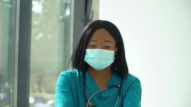 Jovem africana médico mulher em azul máscara protetora olhando para a câmera — Vídeo de Stock