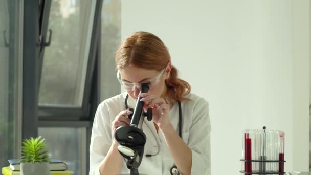 Female scientist doctor doing some research and looking through a microscope in laboratory. Blood test — Stock Video