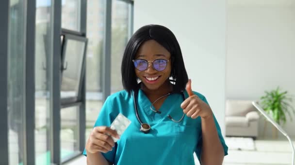 Young african american woman doctor looking at camera and shows pills. Smiling female physician posing in hospital office — Stock Video