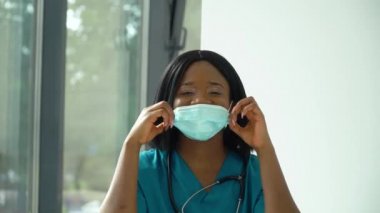 Genç Afrikalı Amerikalı kadın doktor hastanede tıbbi maskesini çıkarıyor.