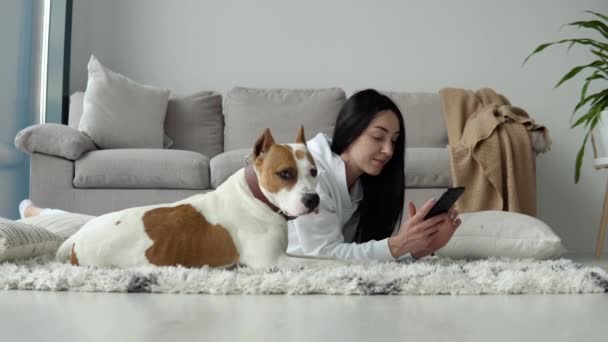 Mujer joven que se relaja con su perro y el uso del teléfono en un hermoso apartamento moderno — Vídeos de Stock