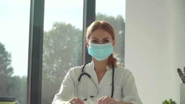 Jeune femme médecin en masque de protection bleu regardant la caméra — Video