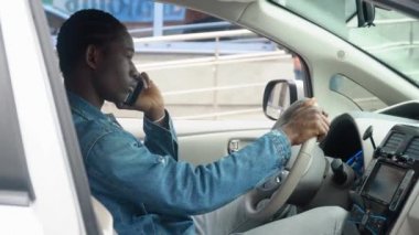 Afrikalı Amerikalı bir adam lüks bir arabada telefon görüşmesi yapıyor.