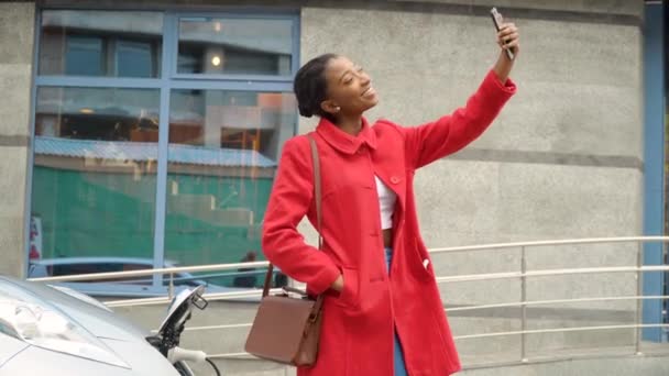 Afro-américaine fille prendre selfie avec voiture électrique qui charge. Recharge de voiture électrique. Transport respectueux de l'environnement — Video