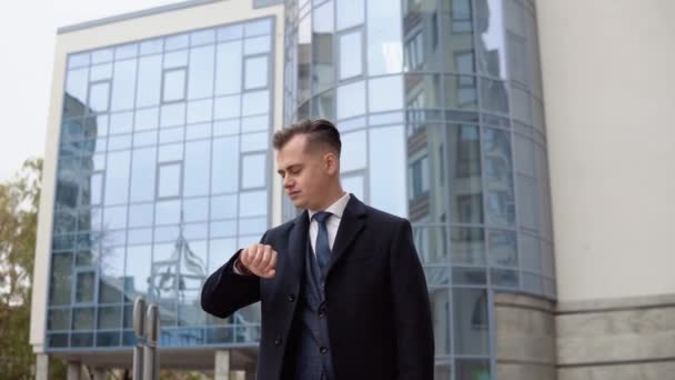 Joven y elegante hombre de negocios con chaqueta azul y abrigo cerca del centro de oficinas esperando una reunión de negocios — Vídeos de Stock