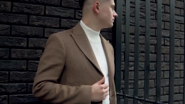 Beau homme à la mode en manteau marron sur un fond de mur de briques. Nouvelle collection de vêtements tendance — Video