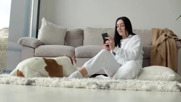 Giovane donna che si rilassa con il suo cane e utilizzare il telefono in un bellissimo appartamento moderno — Video Stock