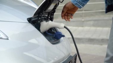 Siyah adamın elleri şarj olmak için elektrikli arabasını kapatıyor.