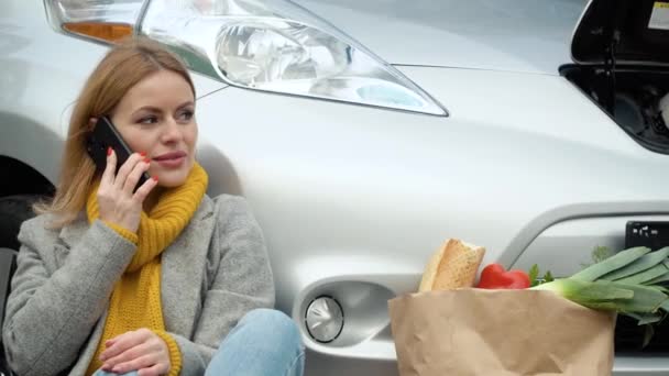 Mujer hablando por teléfono mientras carga un coche eléctrico en el estacionamiento. Transporte respetuoso con el medio ambiente — Vídeos de Stock